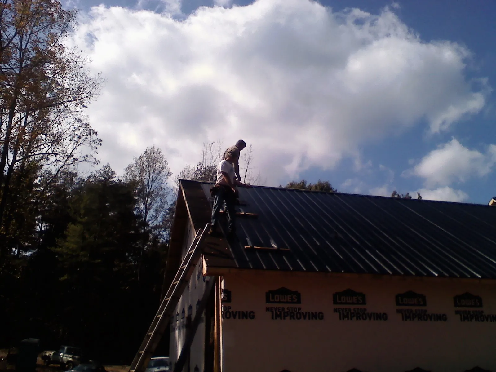 Roofer fastening dark metal panels high against a cloudy sky, from a Roof Inspection job in Rancho Santa Margarita